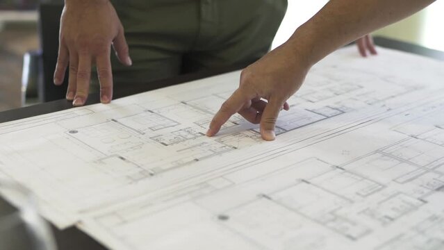 An architect details the intricate plan of a home, his finger guiding through every corner and curve