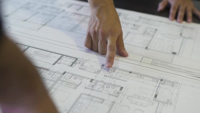An architect traces the outline of a house plan, guiding us through the blueprint of a dream home with his finger