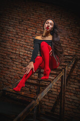 Beautiful young asian girl in black body wear red pantyhose is posing with old wooden step ladder on dark background.