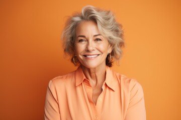 Portrait of smiling senior woman looking at camera isolated on orange background