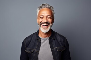 Handsome mature man laughing and looking at camera while standing against grey background