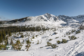 Sceneria roztaczająca się ze szlaku prowadzącego z Hali Gąsienicowej, nad Czarny Staw Gąsienicowy w Tatrach Wysokich. Zdjęcie wykonane w słoneczny, zimowy dzień.