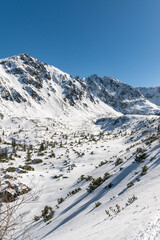 Sceneria roztaczająca się ze szlaku prowadzącego z Hali Gąsienicowej, nad Czarny Staw Gąsienicowy w Tatrach Wysokich. Zdjęcie wykonane w słoneczny, zimowy dzień.