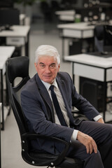 Portrait of a confident mature business man sitting in a chair in the office. Vertical photo.