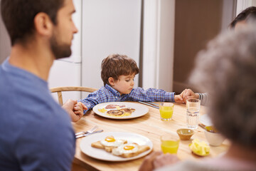 Home, family and praying for breakfast, holding hands and table in kitchen with father, son and religion. House, boy and man worship for eating, bread and juice for diet, healthy and gratitude