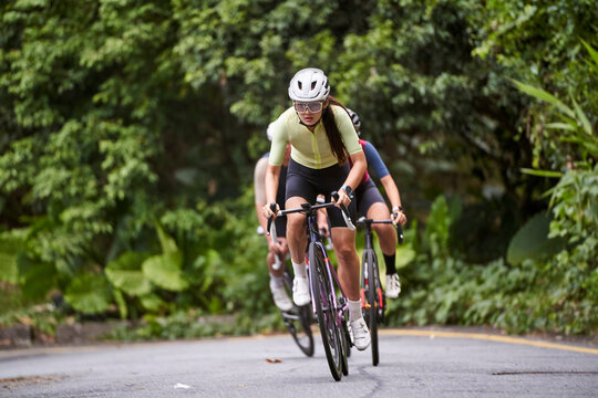 team of young asian adult cycling athletes riding bike outdoors on rural road