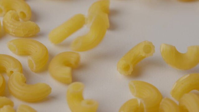 Close-up of dry macaroni pieces tumbling down onto a white surface in soft light