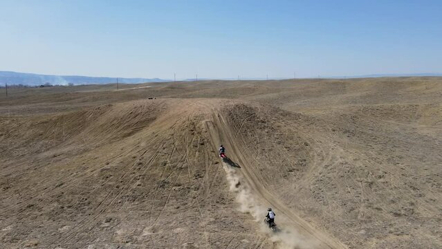 An action-packed, slow-motion drone shot of two motocross riders hitting a big hill jump, in the desert-like terrain of Grand Valley OHV area, located in Grand Junction, Colorado.