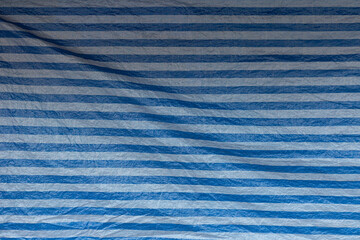 Front view of wrinkled tarp with blue and white stripes. Abstract high resolution full frame...