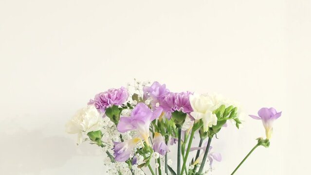 Beautiful bouquet of carnation and freesia close up. White and purple flowers in vase on white background. Natural decoration. Spring fresh floral video