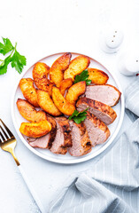 Baked pork tenderloin with caramelized apples on plate, white table background, top view