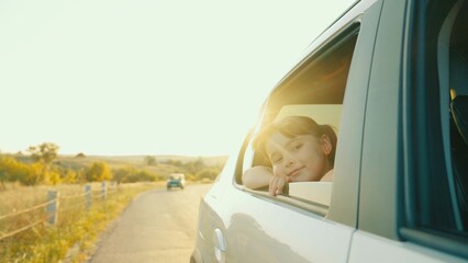 child girl face looks smiling from car out window, summer vacation mood, fresh air vacation, hand, child sitting child car seat, movement child girl hand from window, directing sun glare, schoolgirl
