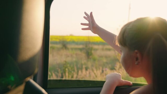 child girl face looks smiling from car out window, little girl sitting car, tourism, beautiful girl sitting back seat with her hand out window catching car sparkles, kid smiling window, child pulls