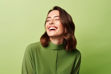 Happy young woman laughing and looking at camera over green background. Emotions concept