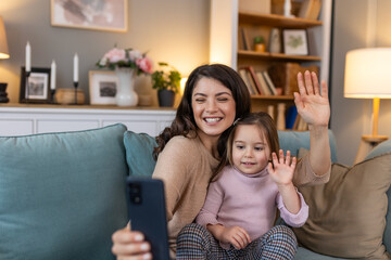 Happy mother and kid daughter waving hands looking at phone camera for video call, smiling mom and...