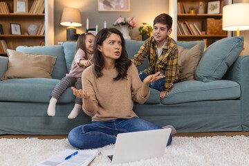 Small mischievous kids noising and distracting mother freelancer trying to concentrate on laptop...