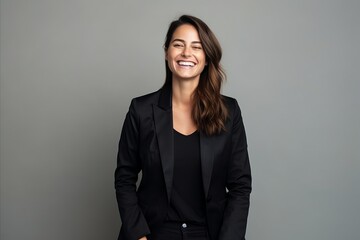 Portrait of a smiling businesswoman in black suit against grey background