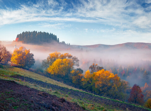 Foggy autumn view of mountain countryside. Calm dawn in Carpathian mountains, Bukovets' village outskirts, Ukraine, Europe. Trees covered with orange and crimson leaves..