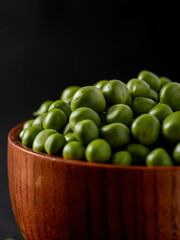 Open pod of young green peas with round peas close-up,Indoor black background and wooden bowl