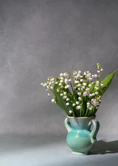 Fotobehang A small bouquet of fresh spring flowers. Lilies of the valley in a light vase isolated on a gray background. Lots of space for text. still life, postcard, gift © Alexander