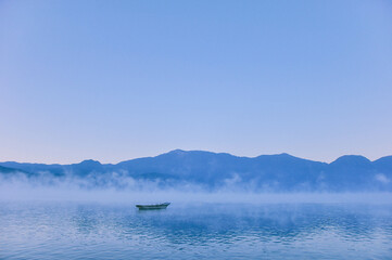 A small wooden fishing row boat on Lugu Lake during a calm Sunrise. Picturesque scenery of the Lugu...
