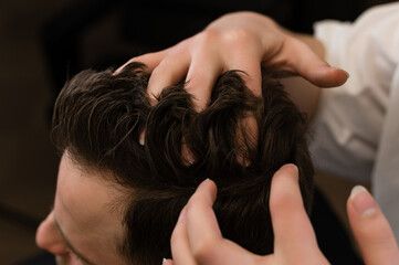 Naklejka premium Haircut of a visitor in a barbershop. Hair styling with a hand, combing the client's hair by a stylist.