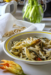 A pasta dish sits on a table beside a flower, blending food with decoration