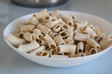 A white bowl containing pasta sits on a wooden table