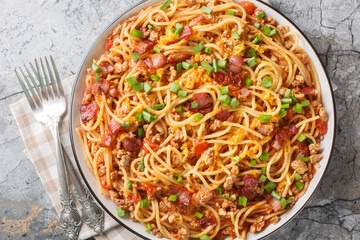 Cowboy spaghetti is made with fire-roasted tomatoes, ground beef, bacon, and cheddar cheese closeup on the plate on the table. Horizontal top view from above