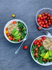 Two bowls of superfood dish with rice, avocado, tomatoes, and spinach on a table