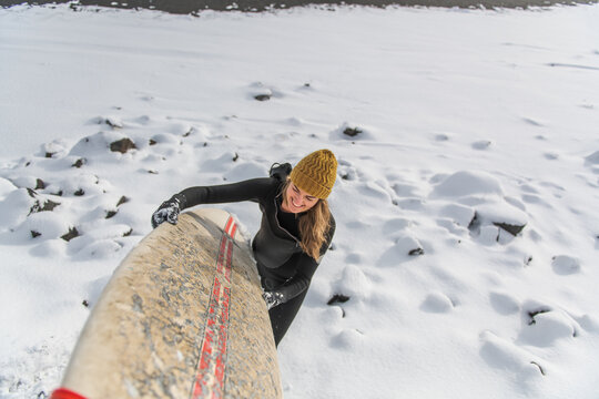 woman holding on surf board on snowy beach winter iceland
