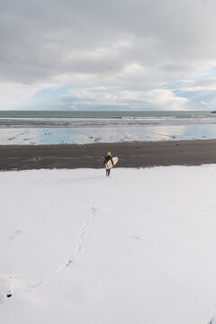 Woman walking on beach with surf board winter iceland