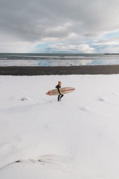 Woman walking on beach with surf board winter iceland