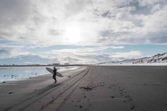Woman walking on beach with surf board winter iceland