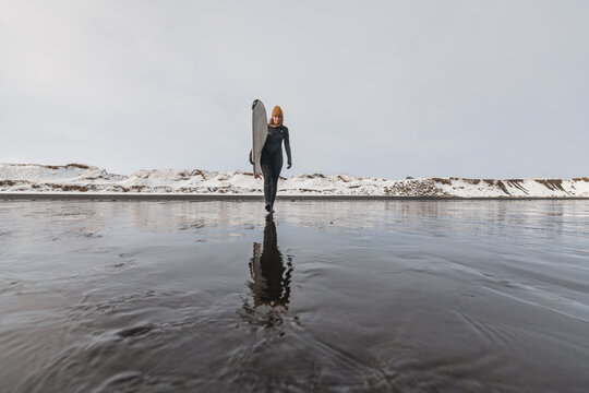 Woman walking on beach with surf board winter iceland