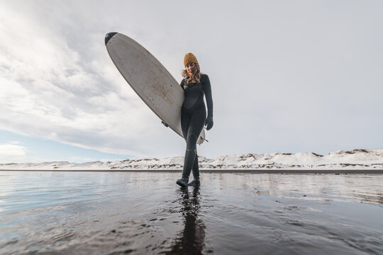 Woman walking on beach with surf board winter iceland