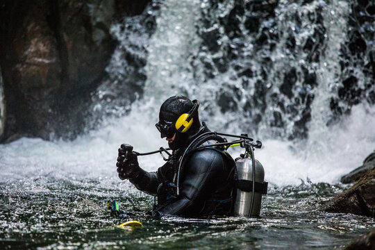 Scuba diver checks regulator prior to diving under a waterfall