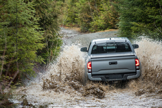Rear view of 4x4 truck driving through water on a gravel road