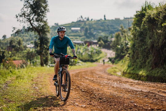 male cyclist bikes up dirt road on Congo Nile Trail in Rwanda