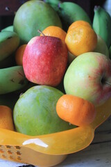 Bananas, oranges, mangoes and apples in plastic containers on the table