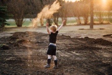 Wide rear view of young boy playing outside and throwing dirt in yard