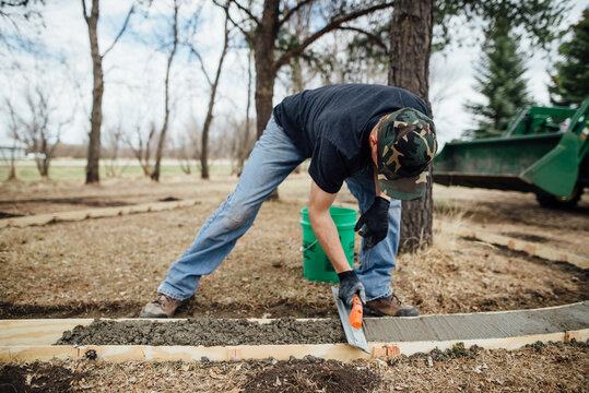 Front view of man using trowel to smooth wet concrete in forms