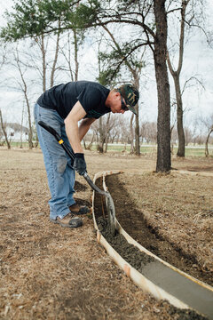 Side view of man working to pour concrete into forms in yard