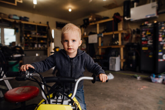 Close up of toddler boy sitting on dirt bike in garage