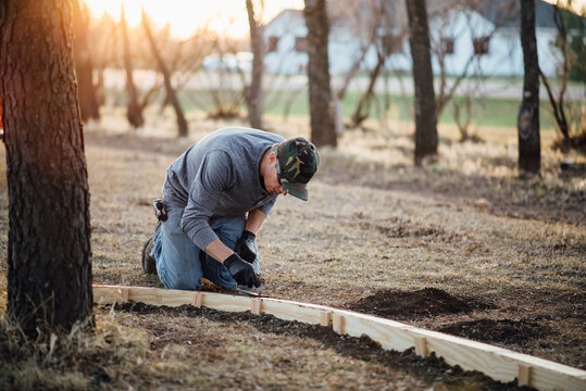 Wide front view of man kneeling while doing manual labor in yard
