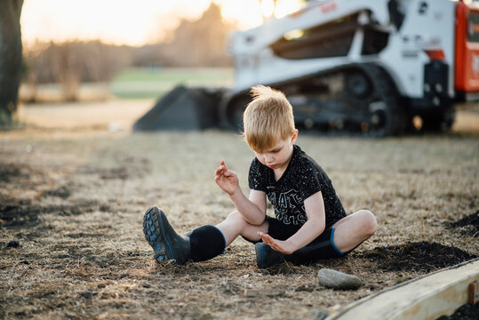 Wide view of young boy sitting on ground and playing with grass