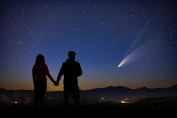 a man and woman stand in awe as they gaze upon the magnificent comet