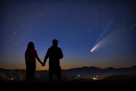 a man and woman stand in awe as they gaze upon the magnificent comet