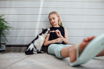 Wide shot of preteen girl holding popsicle for cat to lick.