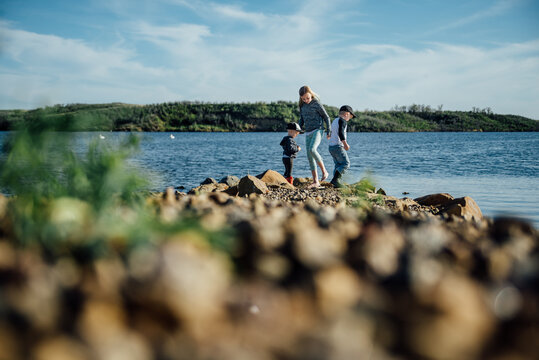 Low wide view of three kids playing on rocky shore of lake.